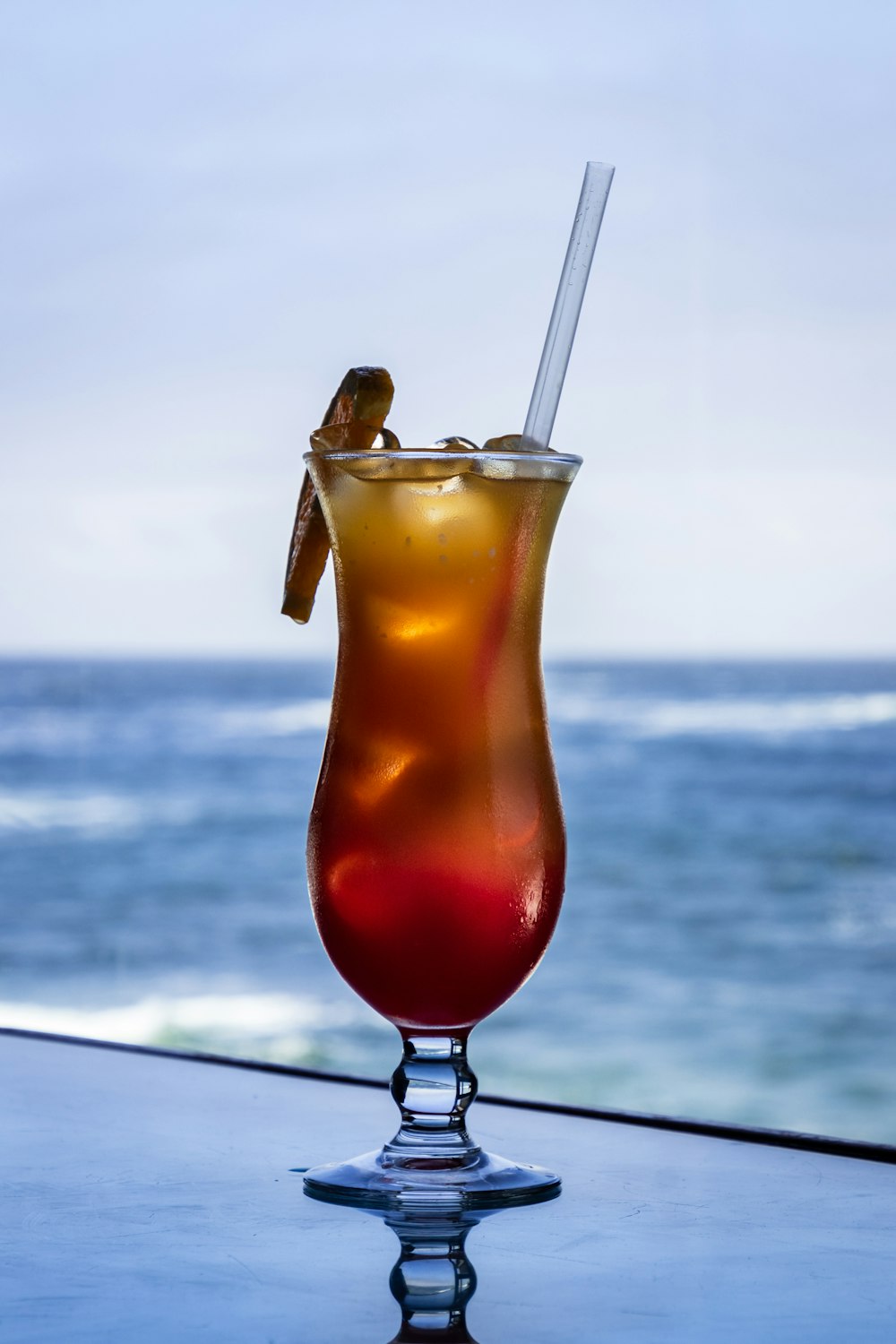 clear drinking glass with orange liquid and straw on white table