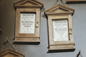 Two framed proclamations are displayed, each encased in wooden frames with glass fronts. The first decree bans all fireworks, while the second restricts the proximity of boys and girls to eight inches of each other. Metal chains are used to hang the frames.