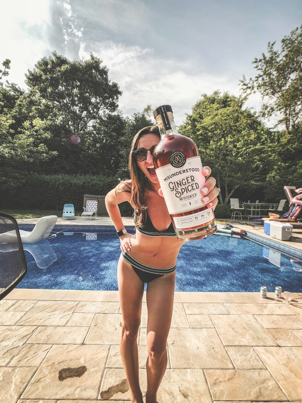 woman in black bikini holding white and red labeled bottle