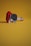 A LEGO-like rendition of a guitar and plectrum placed on a flat surface. The background is a solid mustard yellow, and the guitar pieces are primarily red and white with a black pick.