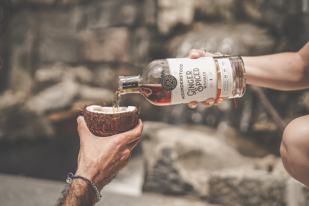 person holding white labeled bottle pouring brown liquid on brown ceramic bowl