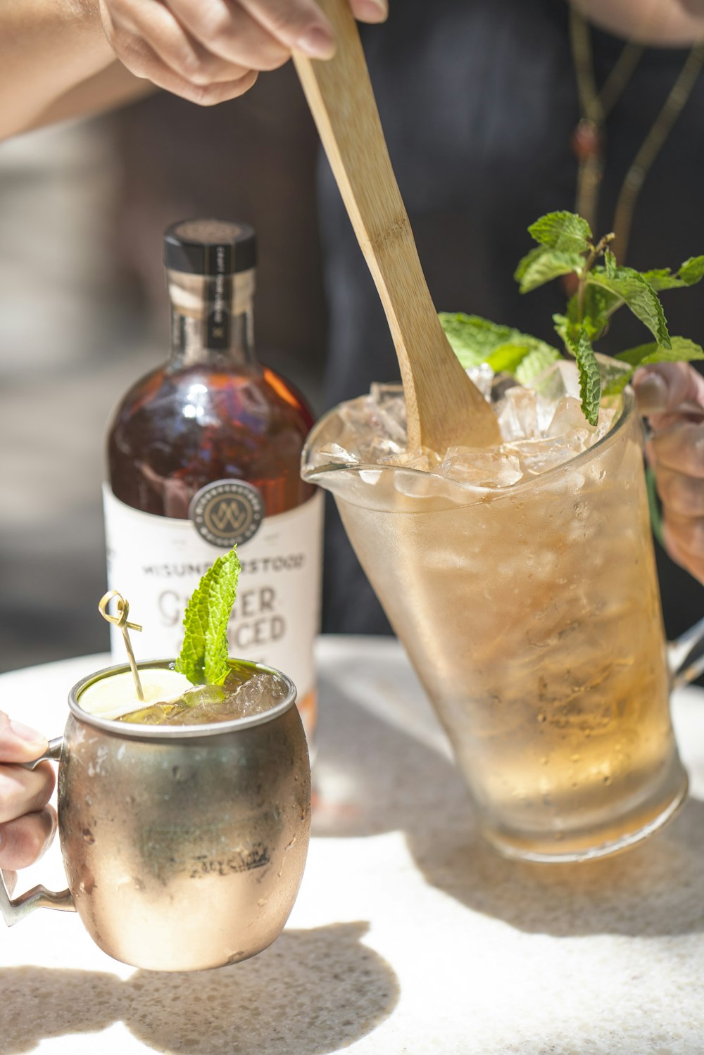 person holding clear drinking glass with brown liquid and ice