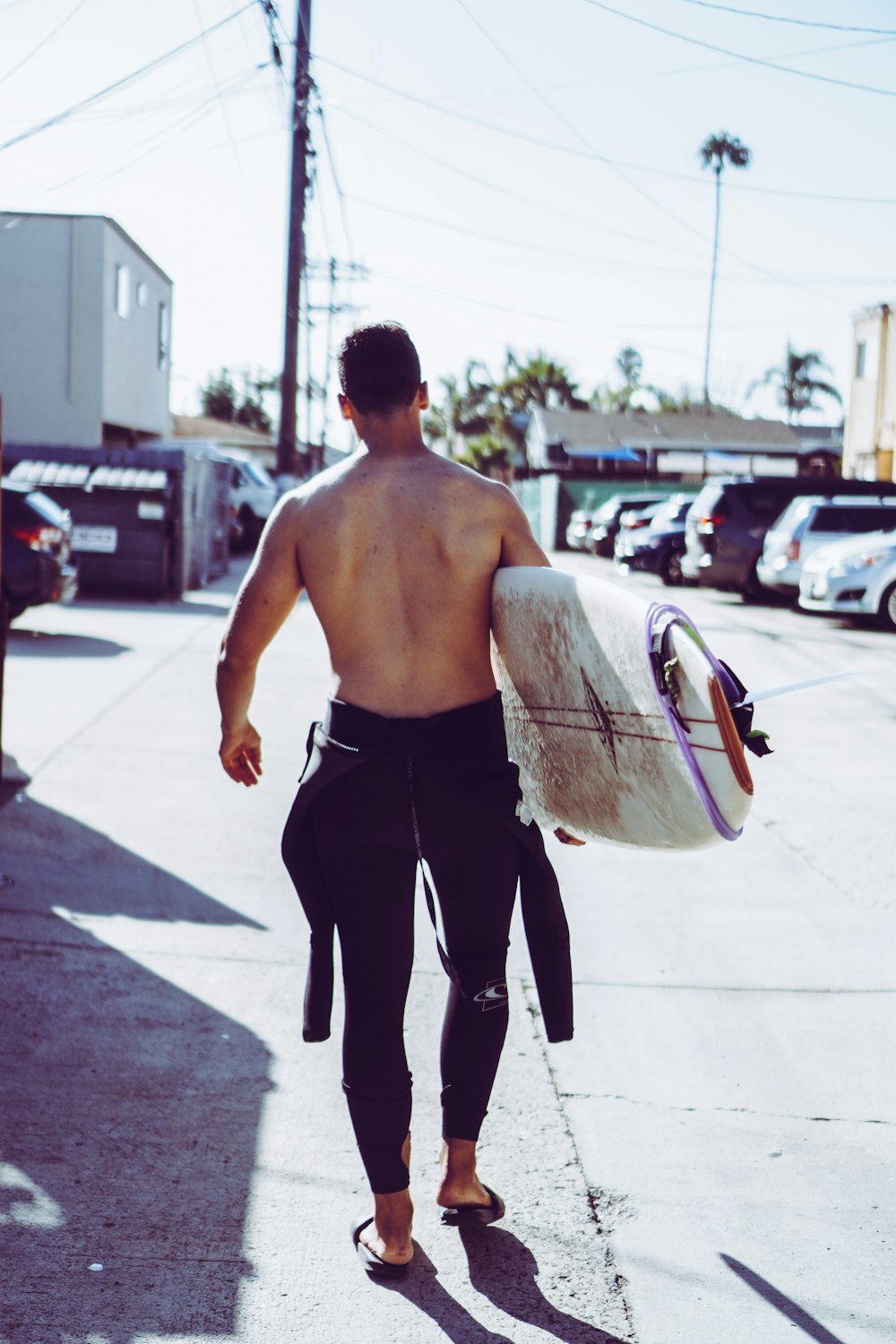 topless man in black pants holding white surfboard during daytime