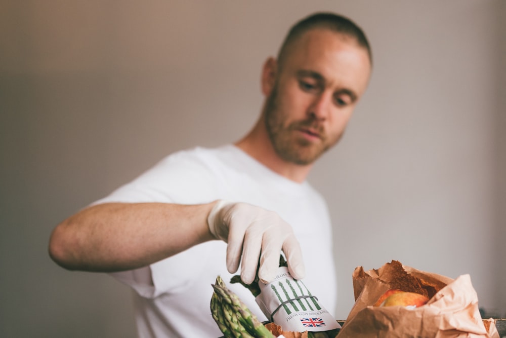 homem na camiseta branca do pescoço da tripulação segurando o vegetal verde