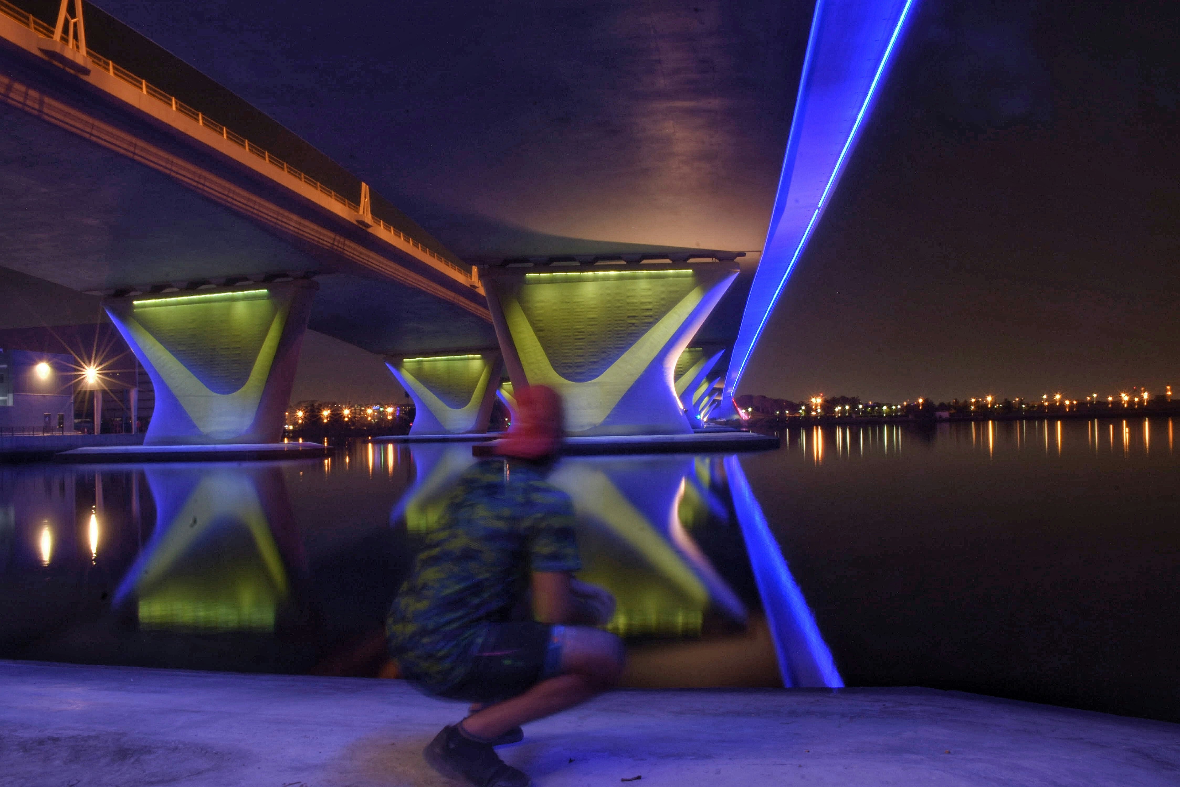 man in green and blue jacket sitting on gray concrete floor near body of water during