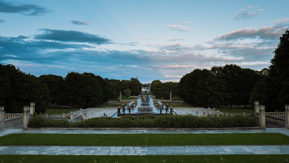 green trees and white fountain under blue sky and white clouds during daytime