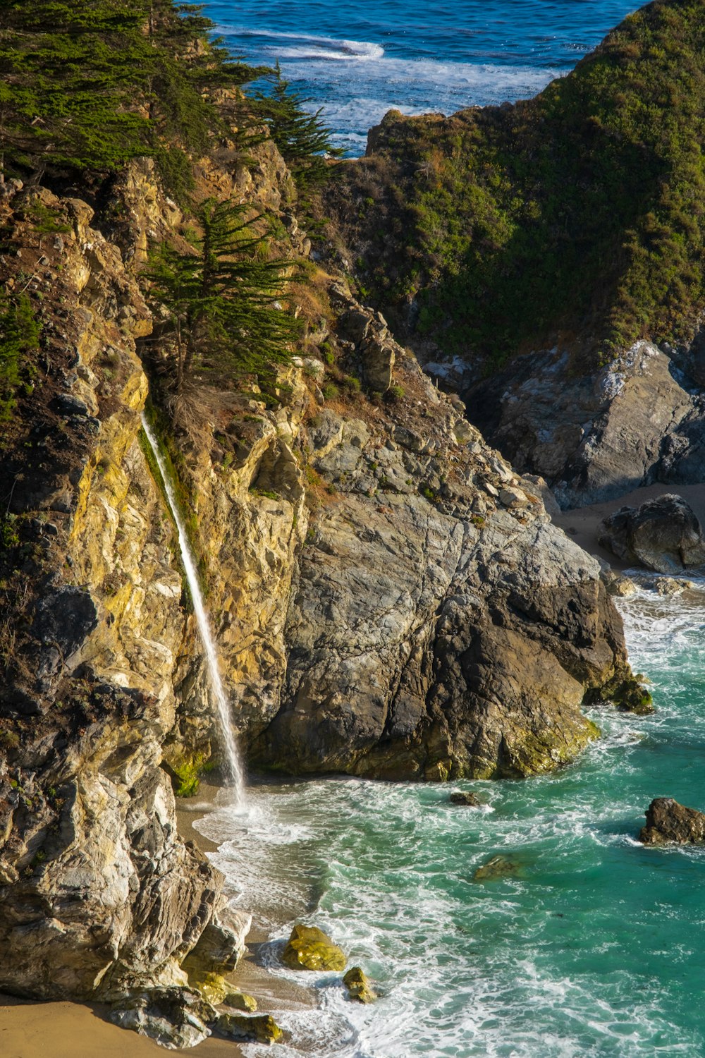 water falls between brown and green rock formation during daytime