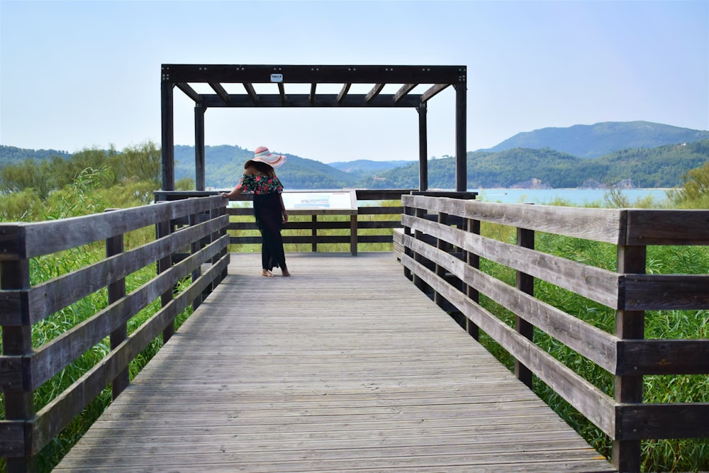 woman in black jacket and black pants standing on wooden bridge during daytime