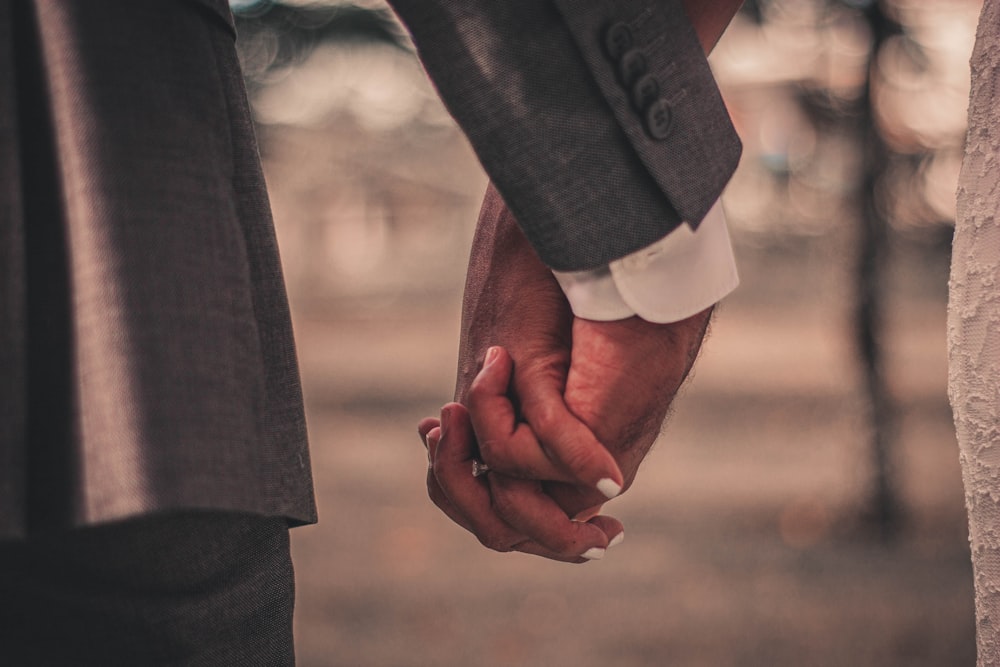 man in black suit jacket holding hands with woman in white long sleeve shirt