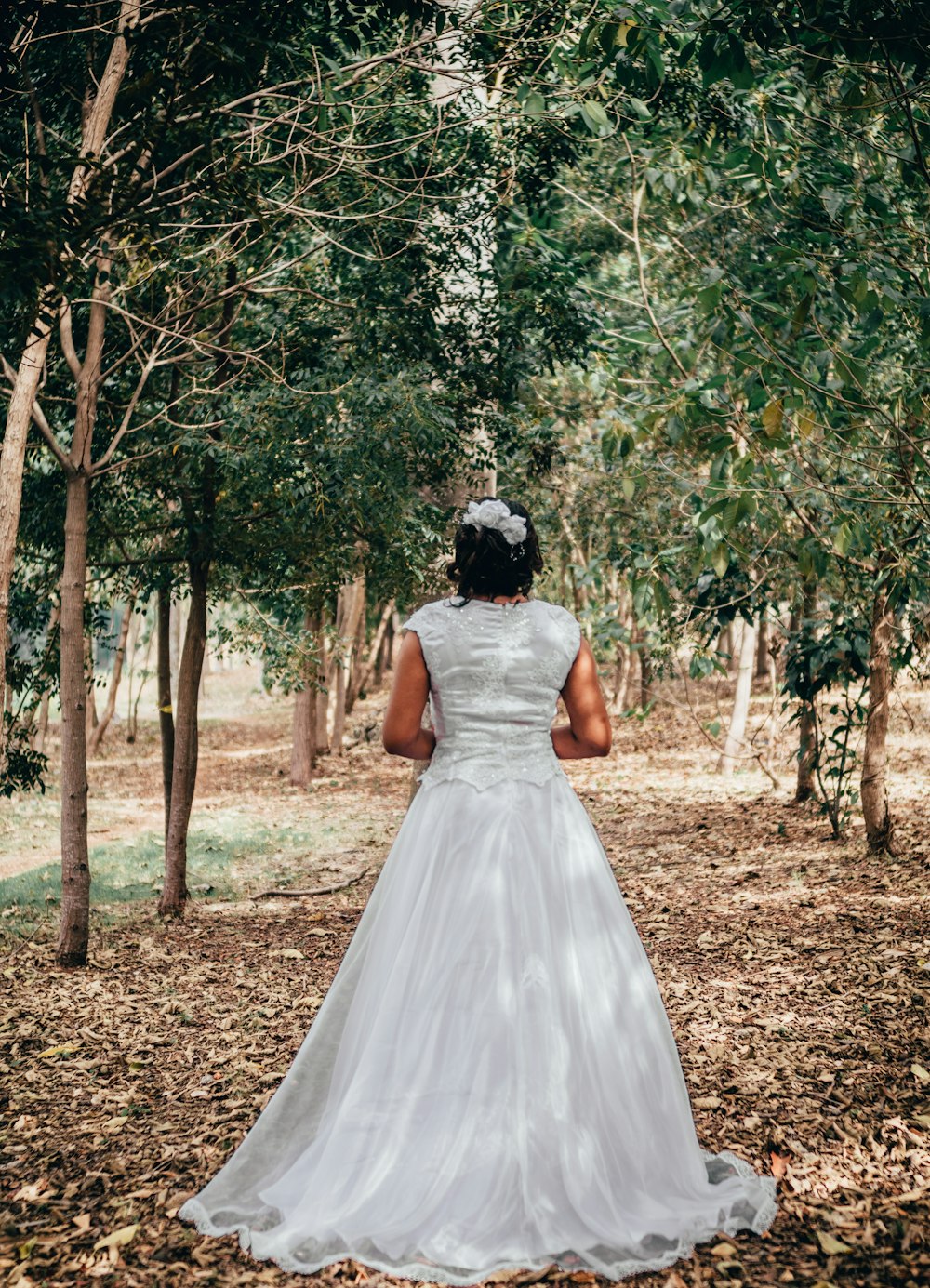 woman in white wedding dress standing on brown soil surrounded by green trees during daytime