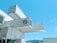 A modern building constructed from stacked shipping containers, adorned with the logo of a popular coffee chain. The containers are painted white and configured in an innovative design, standing out against a clear blue sky. A staircase and railing are visible, providing access between levels.