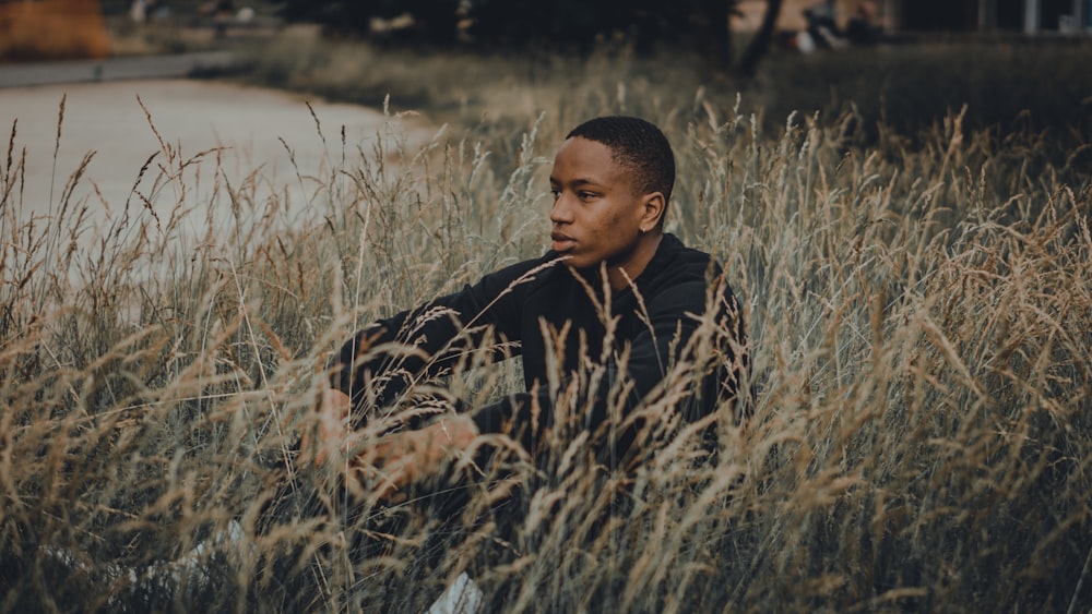 man in black jacket sitting on grass field during daytime