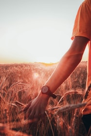person in orange t-shirt wearing black watch standing on brown grass field during daytime