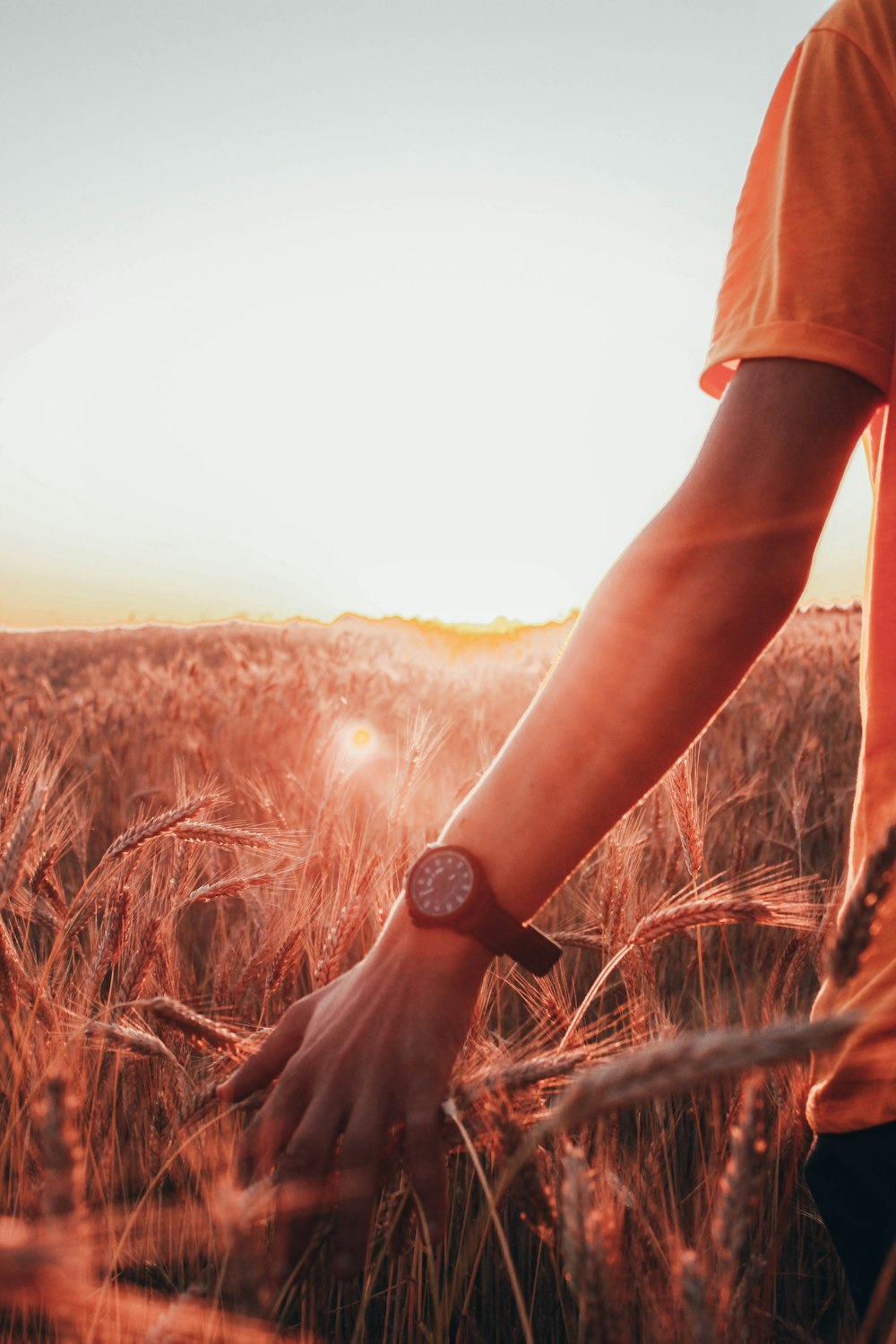 personne en t-shirt orange portant une montre noire debout sur un champ d’herbe brune pendant la journée