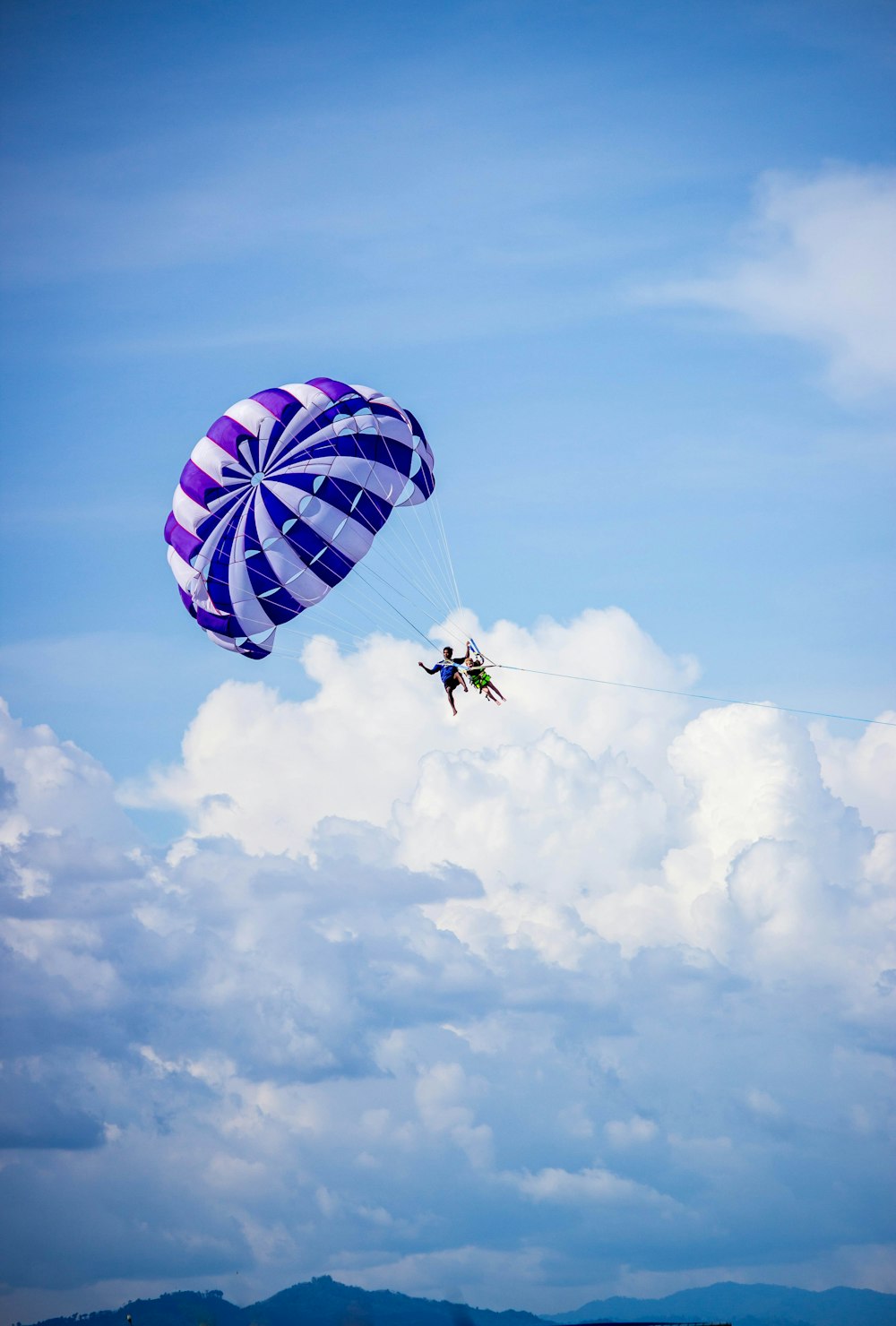 person riding on red and blue parachute under blue sky during daytime