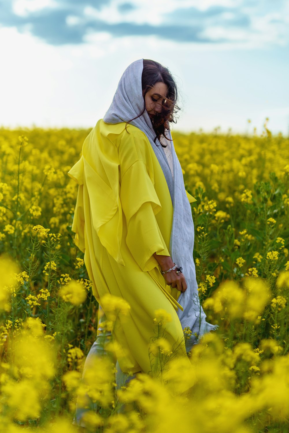 mulher no manto branco que está no campo da flor amarela durante o dia
