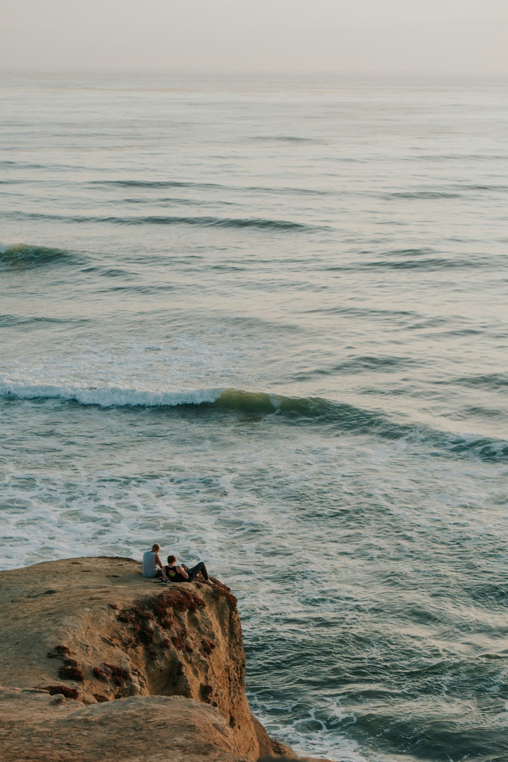 man in black shirt standing on brown rock formation near body of water during daytime