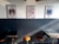 Three colorful posters featuring distinct artistic designs are mounted on a two-tone wall; the lower part is dark, while the top part is light. Below the posters, there are several stools and tables arranged against the wall.