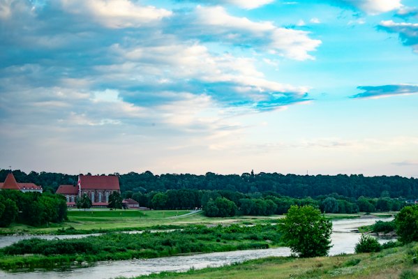Green grass field near body of water under blue sky during daytime — Kaunas, Lithuania