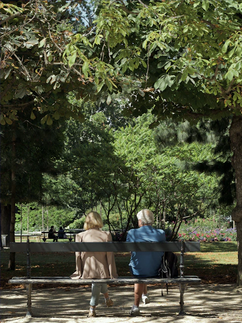 An elderly couple sharing a quiet laugh on a park bench under golden autumn leaves.