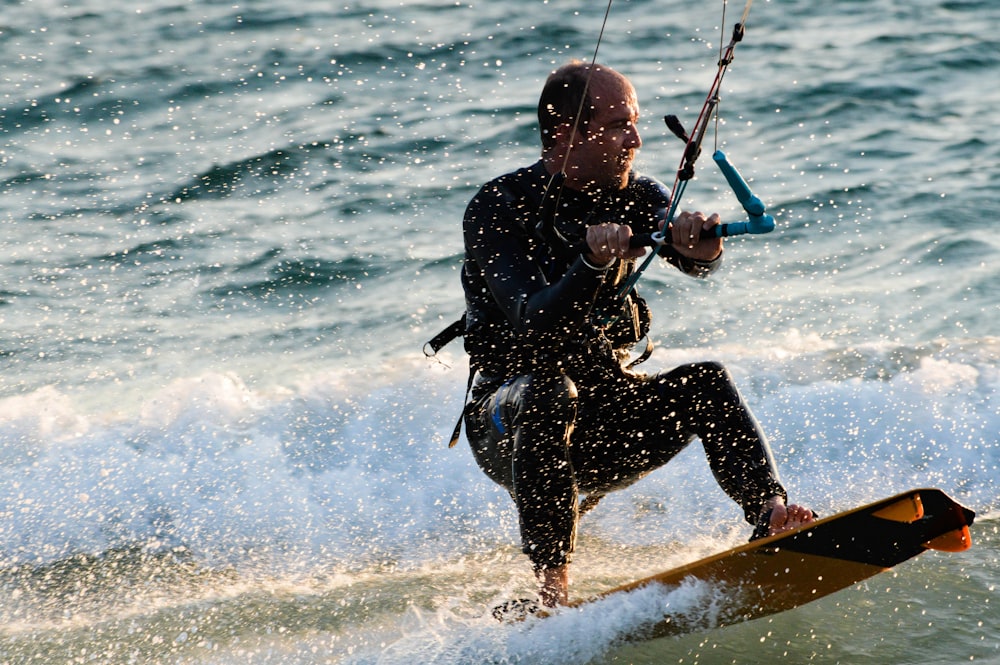 man in black wet suit riding on orange surfboard during daytime