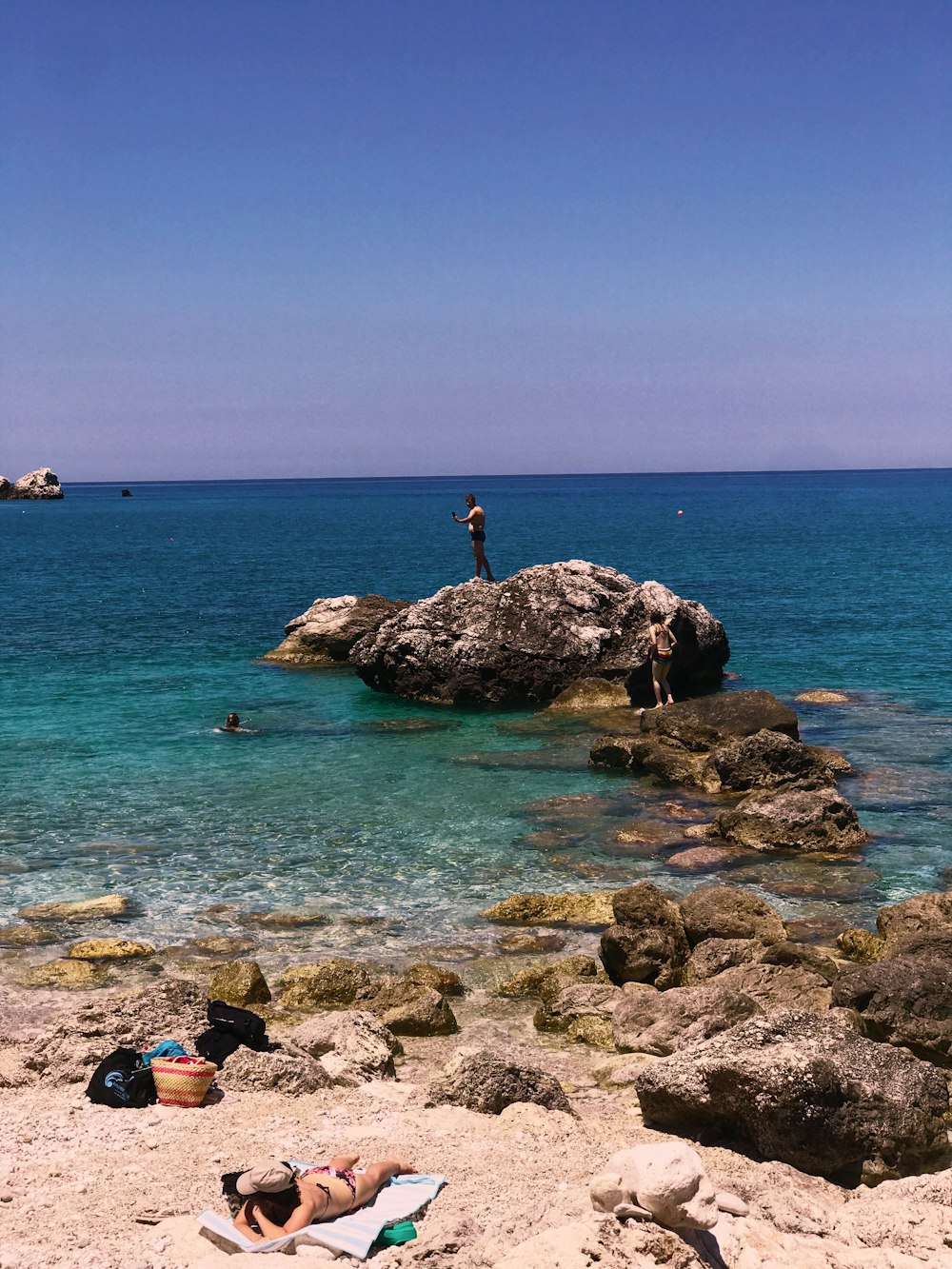 person in black shirt and blue denim jeans standing on brown rock formation on sea shore