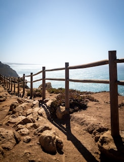 brown wooden fence on brown sand near body of water during daytime