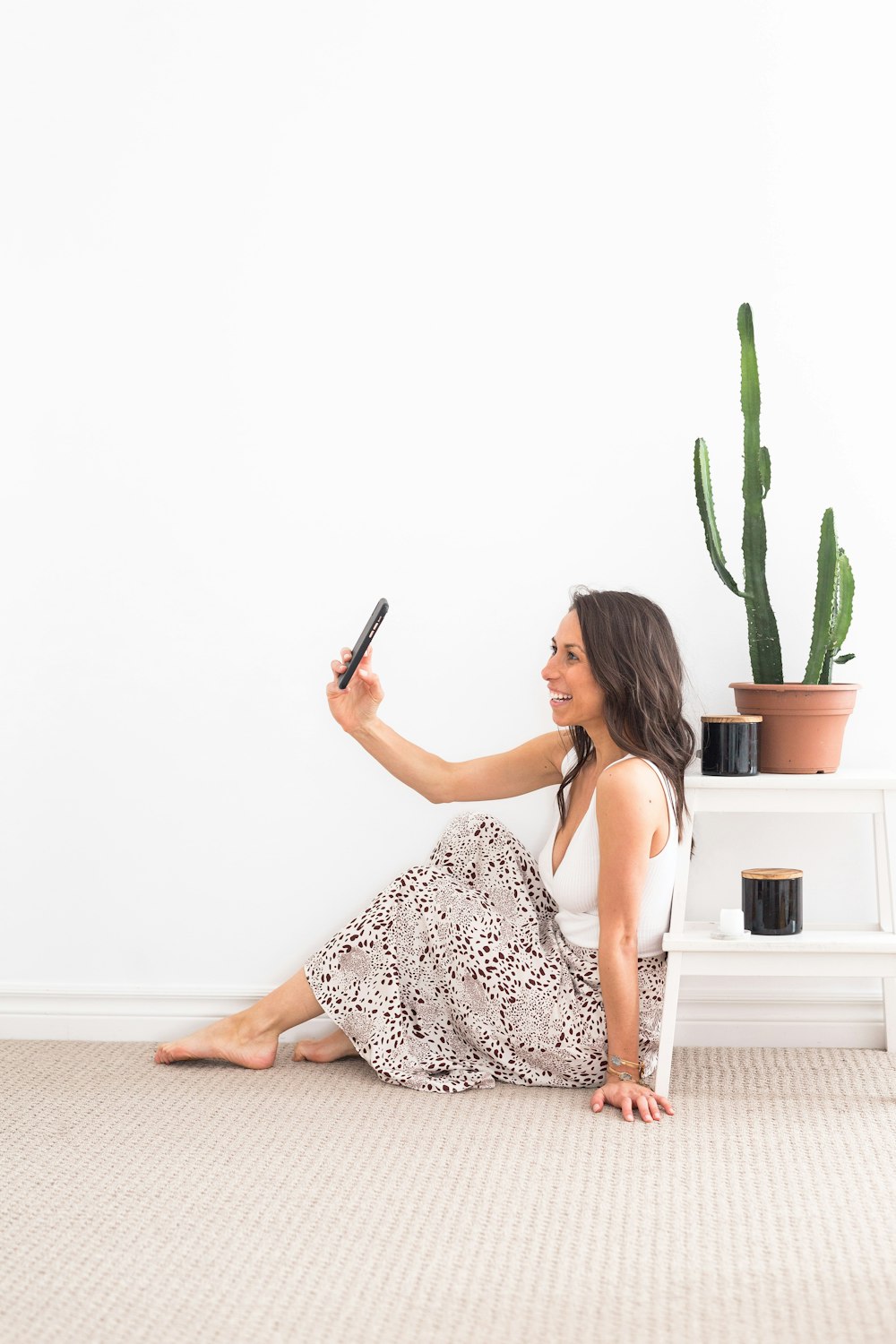 woman in white and black floral spaghetti strap dress holding black smartphone