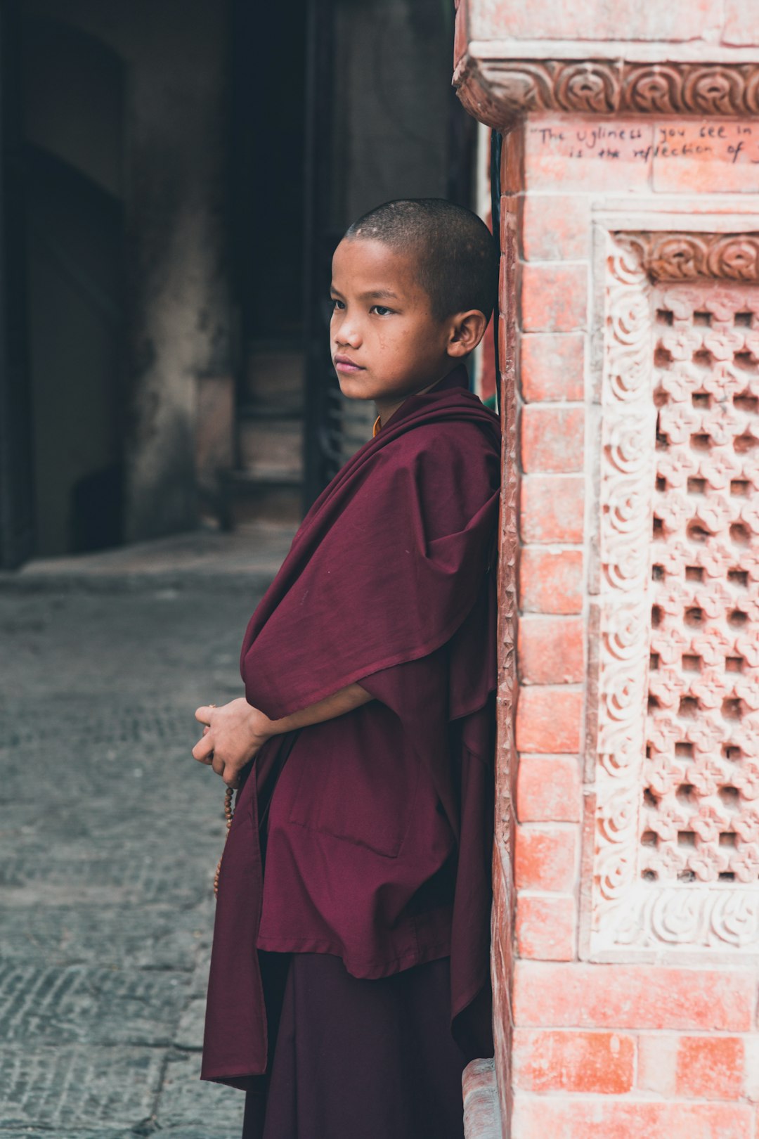 boy in red robe standing near brown brick wall during daytime