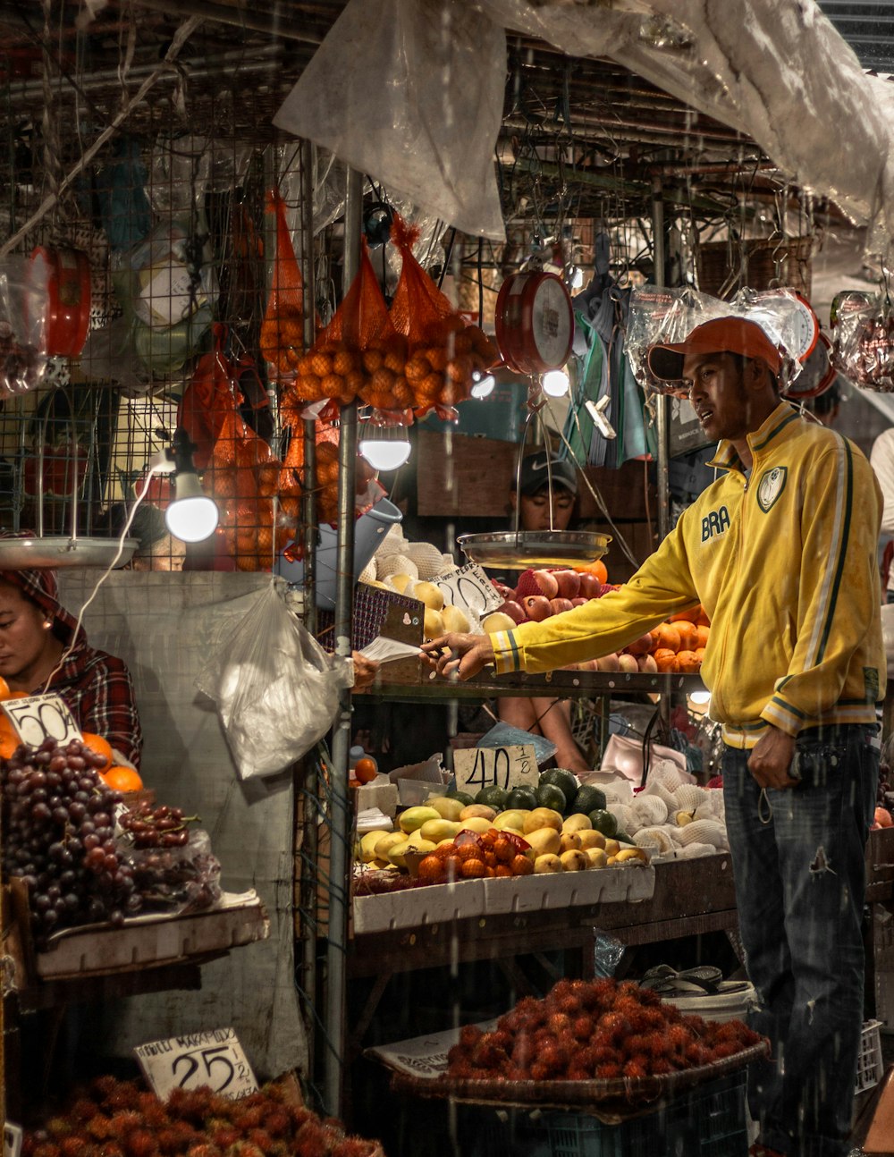 man in yellow polo shirt and blue denim jeans standing in front of fruit stand