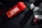 A vibrant red shaker with 'CTRL A Meal Replacement' printed on it rests on a dark surface, accompanied by a gaming controller with red accents and a black microphone on a stand. Part of a keyboard is visible on the left, partially illuminated by red backlight.