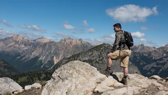 A hiker wearing abrasion-resistant pants and moisture-wicking layers, standing on a rocky mountain trail under a clear sky.