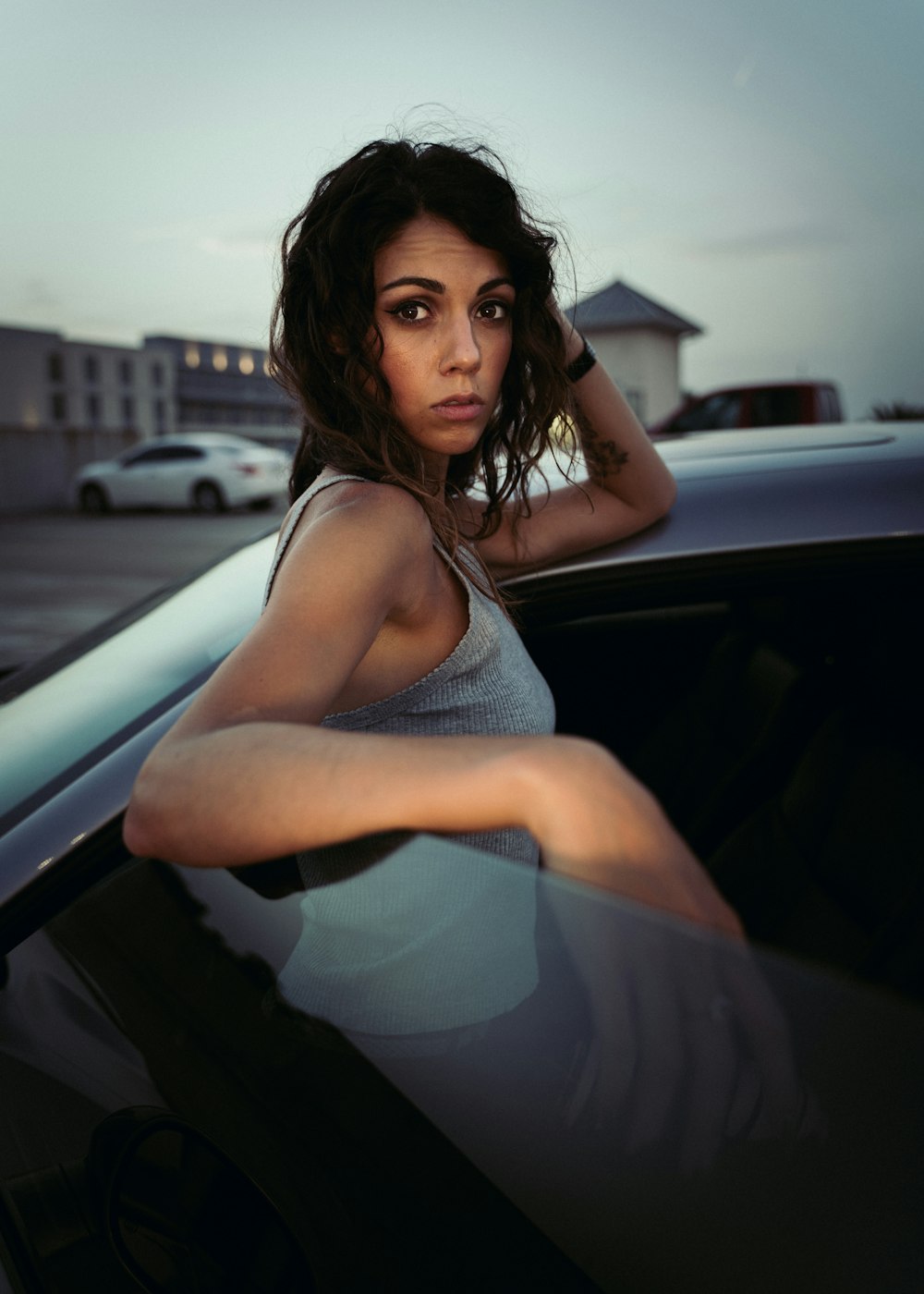 woman in gray tank top sitting on car hood during daytime