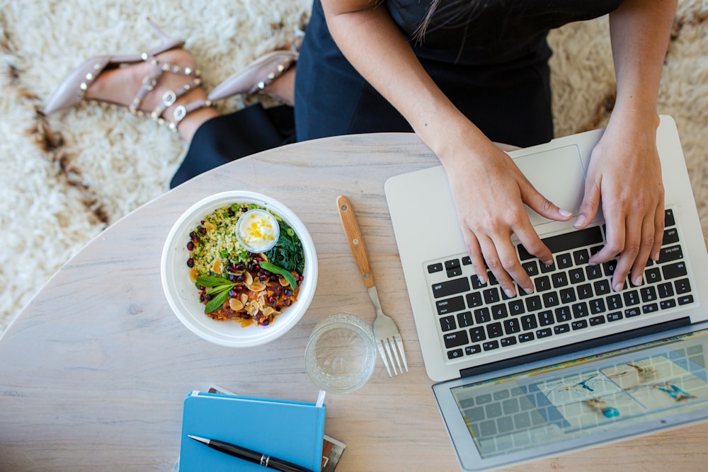 person using macbook pro on brown wooden table