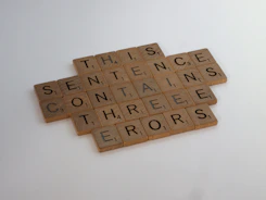 Several Scrabble tiles are arranged on a flat surface. They form the sentence 'THIS SENTENCE CONTAINS THREE ERORS' with a deliberate misspelling of the word 'ERRORS'.
