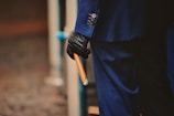 A person dressed in a dark blue suit and wearing black gloves holds a large cigar. The focus is on the details of the suit buttons and the cigar.