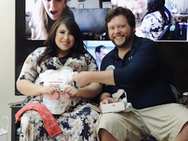 A couple happily opening a personalized digital invitation on a tablet, surrounded by small gift items.