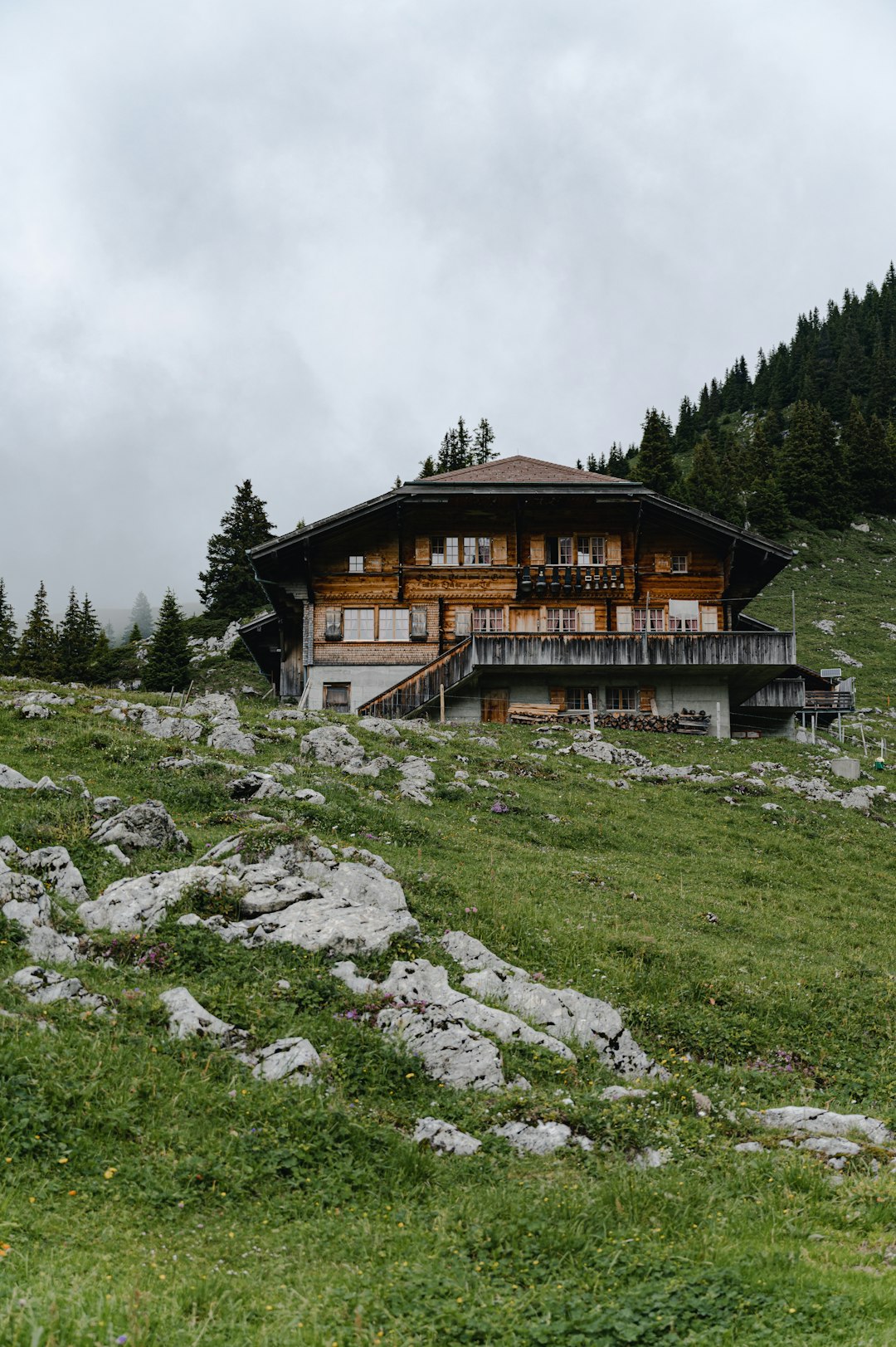 brown wooden house on green grass field near green trees under white clouds during daytime