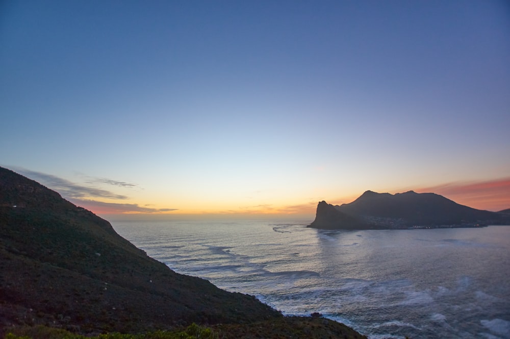 silhouette of mountain near body of water during sunset