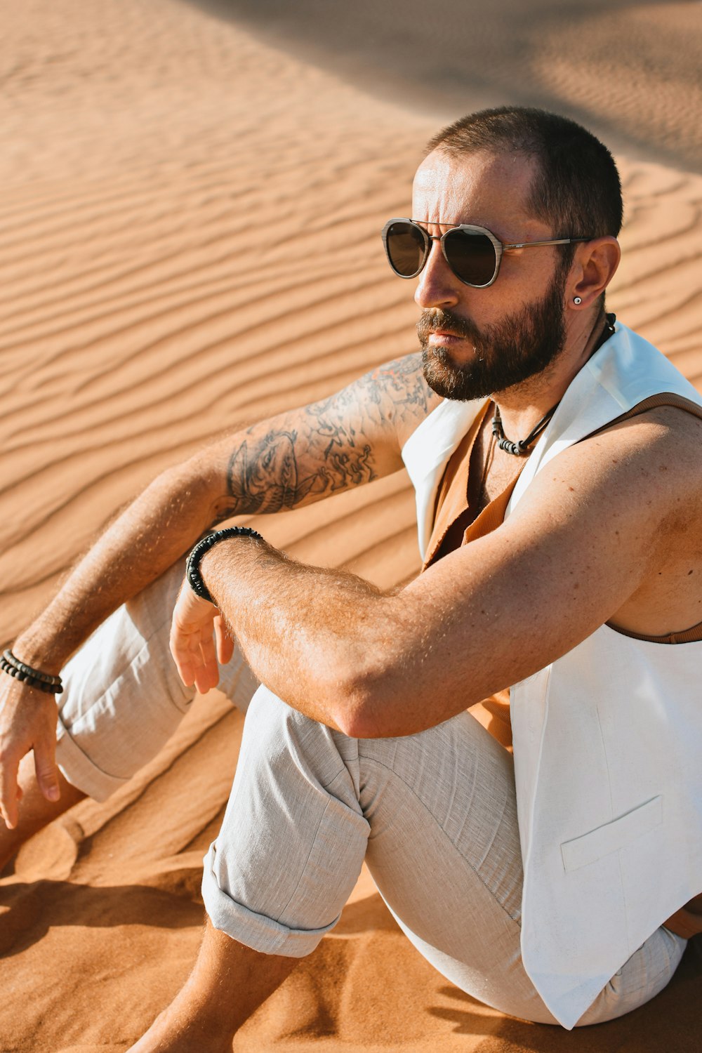 man in white tank top and brown pants wearing black sunglasses sitting on white chair