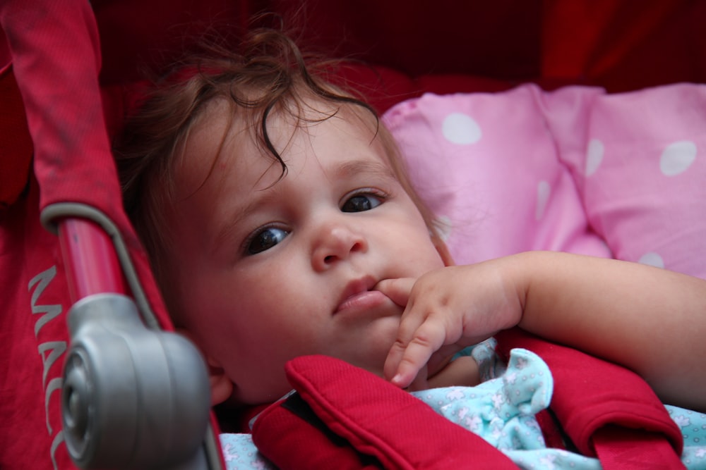 baby in red shirt lying on pink bed