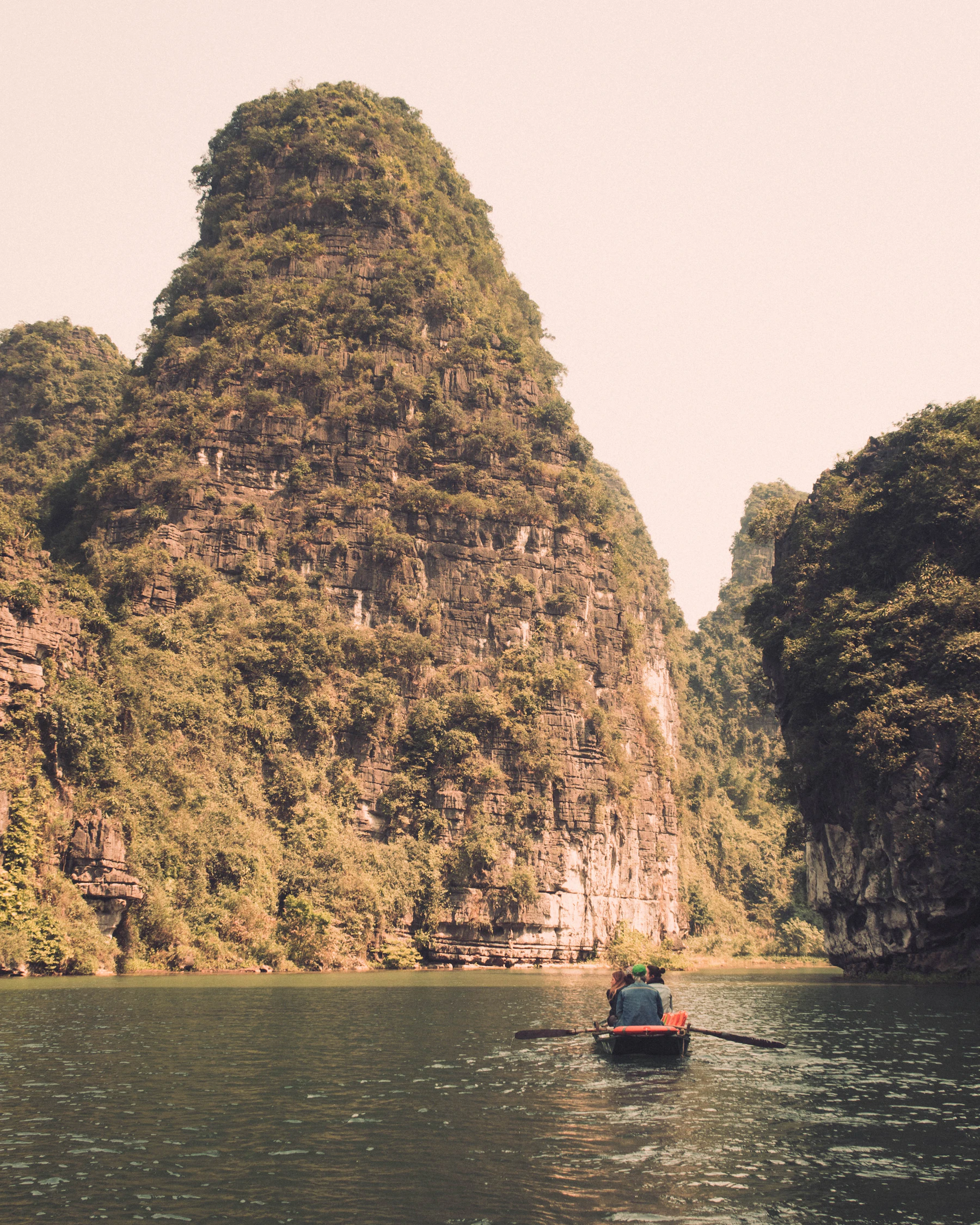 Small boat travelling between limestone cliffs in Trang An, Ninh Binh, Vietnam