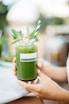 person holding green glass jar with white and blue straw detox juice