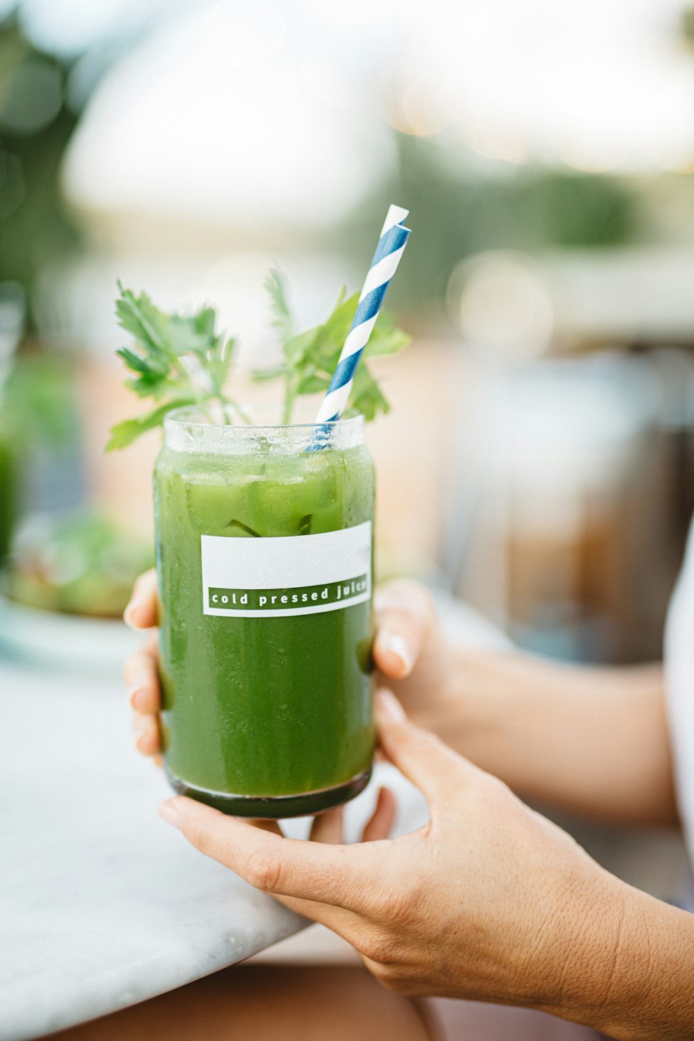 person holding green glass jar with white and blue straw