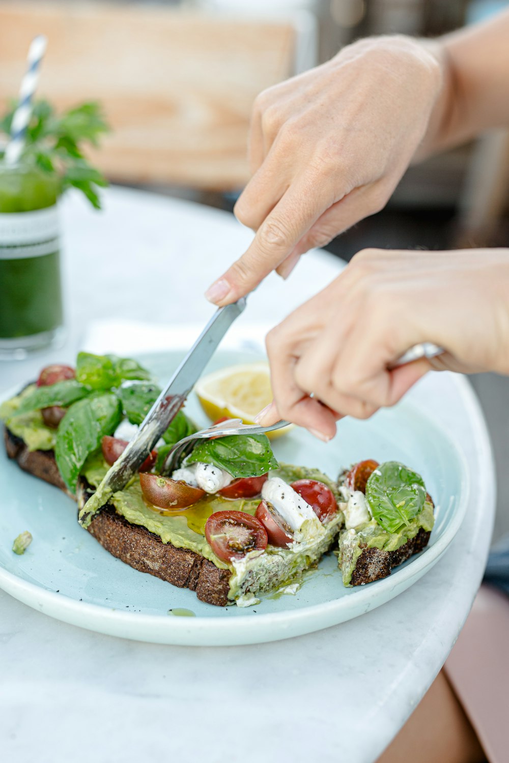 person holding knife slicing bread with vegetable on white ceramic plate