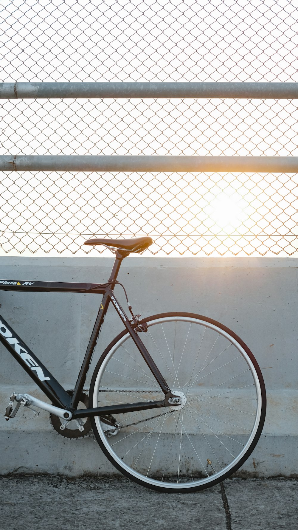 orange and black road bike leaning on white metal fence