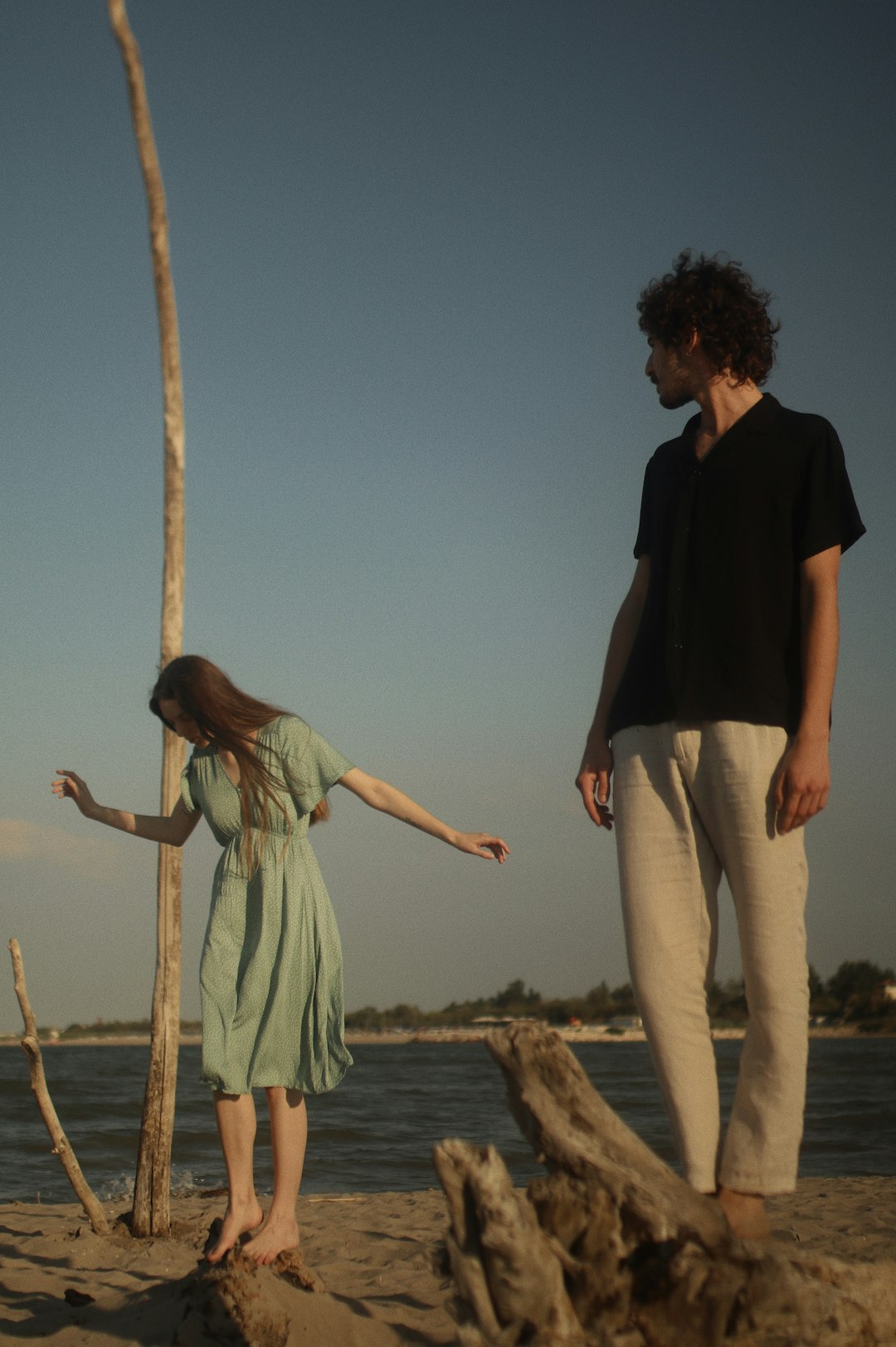 man in black shirt and woman in white dress standing on brown wooden fence during daytime