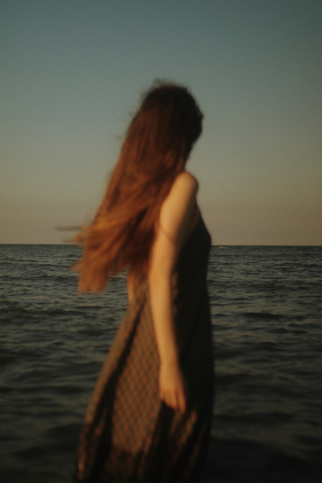 woman in black sleeveless dress standing near body of water during daytime