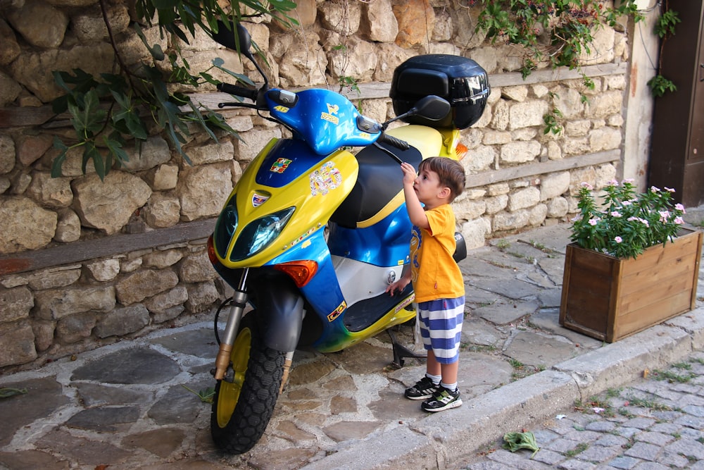 boy in blue and yellow vest riding yellow and black motor scooter