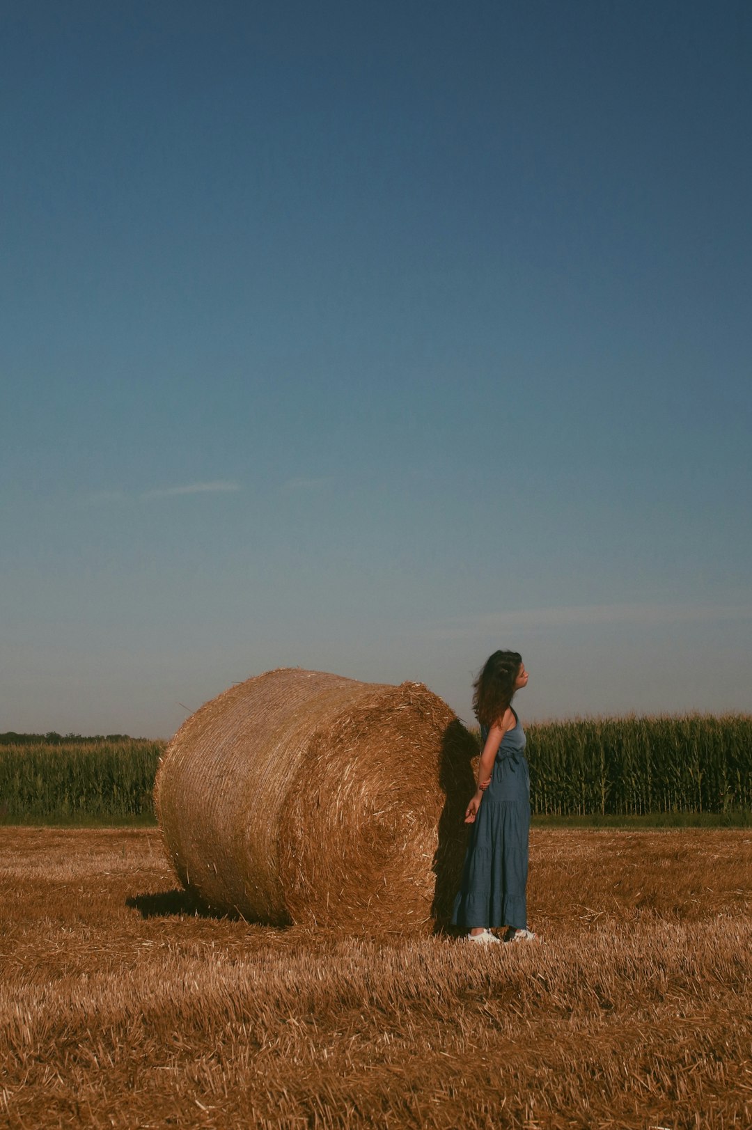 woman in white shirt standing beside brown hay roll during daytime